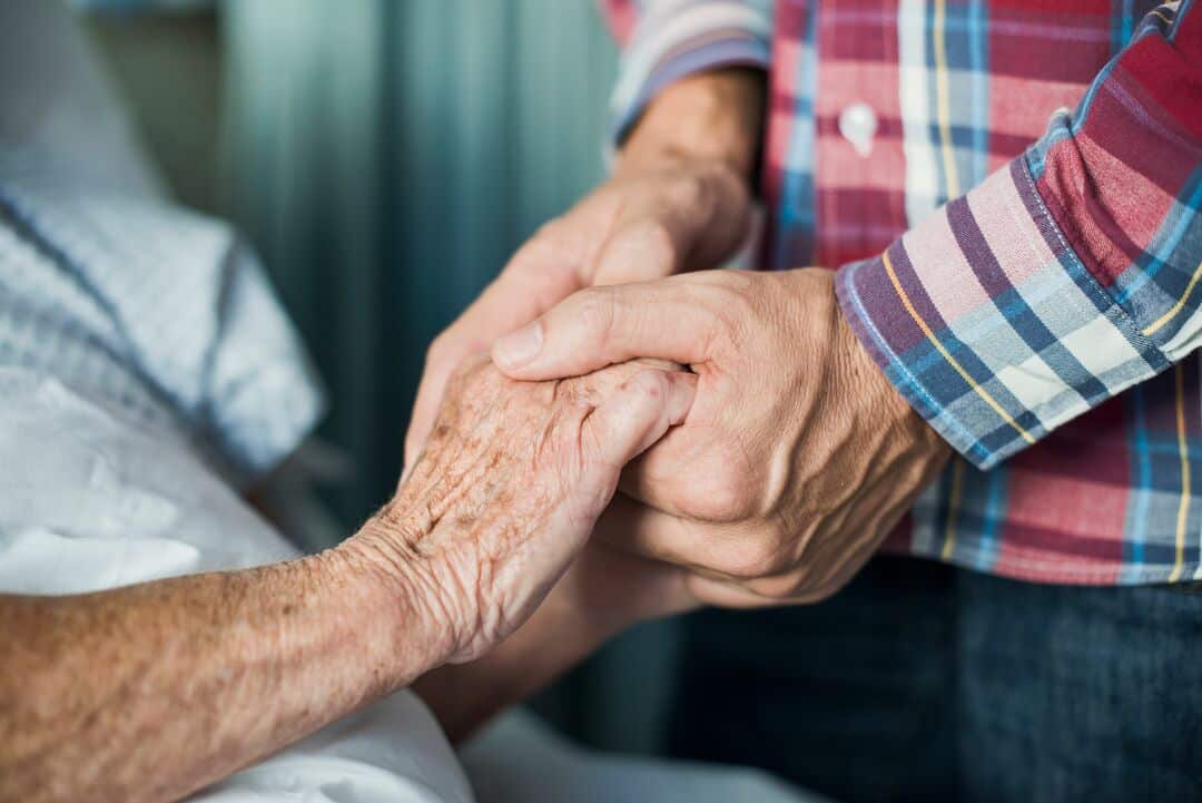 A man holds an elderly patient's hand.